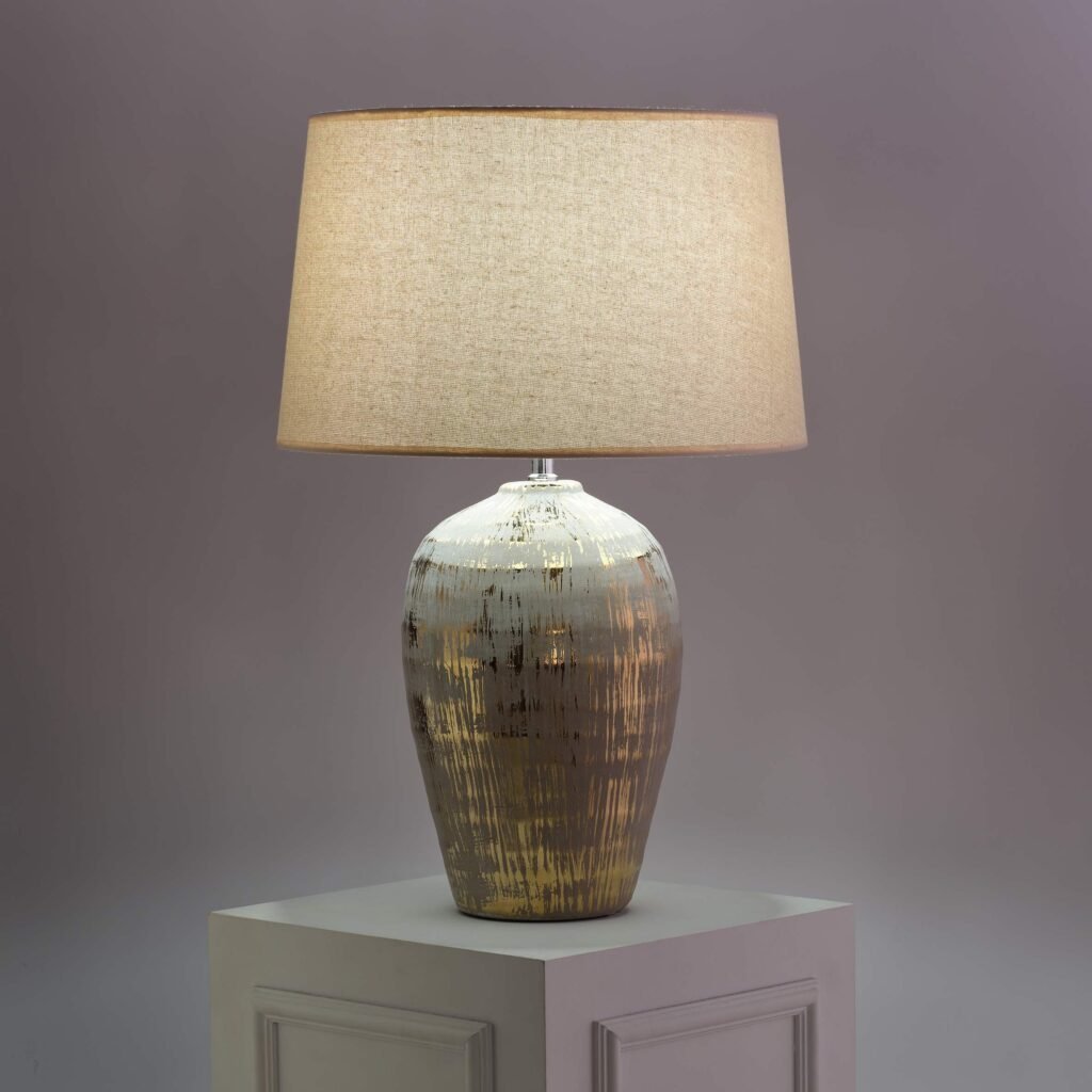 dekoracyjna lampa z metalizowaną podstawą i jasnym abażurem materiałowym
